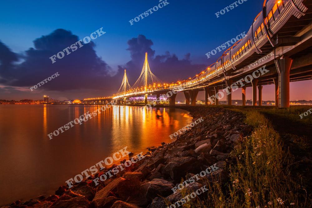 На фотографии изображён Большой Обуховский мост, известный также как Вантовый мост. Этот мост соединяет берега Невы. Вечернее освещение моста подчёркивает его изящные линии и подчёркивает величие конструкции. Вид на мост с воды позволяет оценить его архитектурное совершенство и гармонию с окружающим городским ландшафтом.